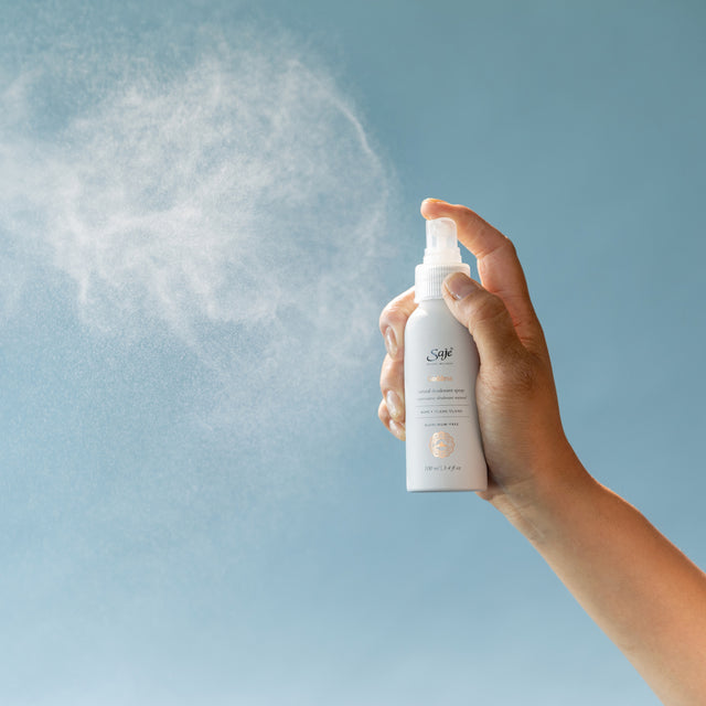 Person spraying deodorant on blue background