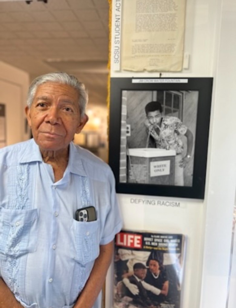Cecil B. Williams in front of portrait of himself drinking from "whites-only" water fountain (photo credit - Martie Bowser)