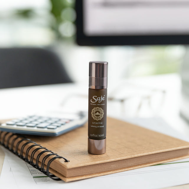 Unwind calming oil blend roll-on placed on top of a notebook 
