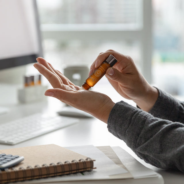 A person applying Unwind calming oil blend roll-on onto their pulse points in their hand